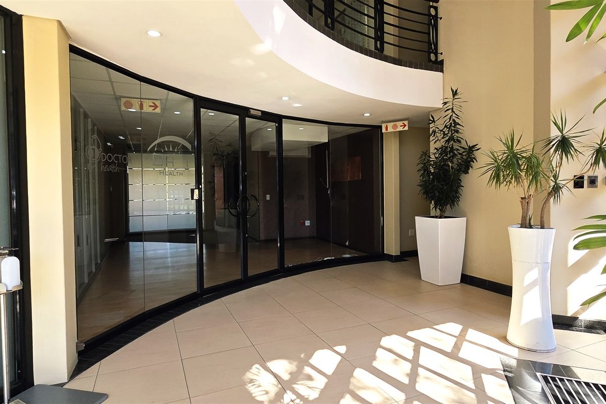 A bright and modern office building entrance featuring tiled floors, a curved glass partition, and a mezzanine level with a metal railing.