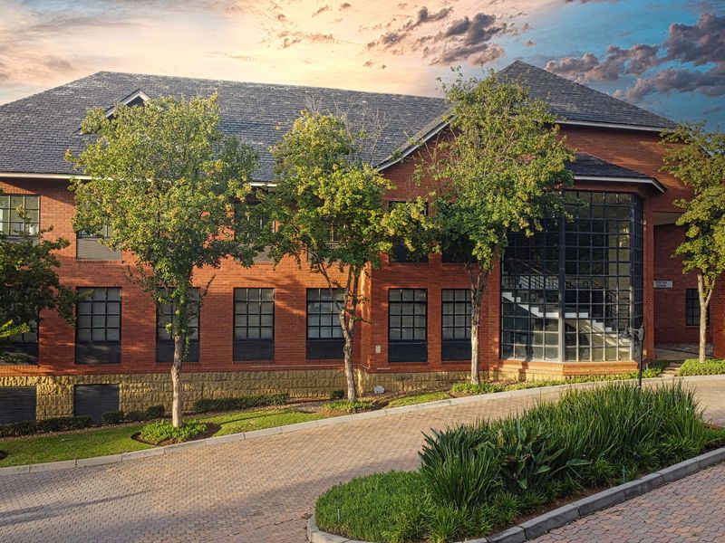 A professional exterior view of a multi-story brick office building featuring large grid-pattern windows, a slate roof, and a well-maintained paved driveway.