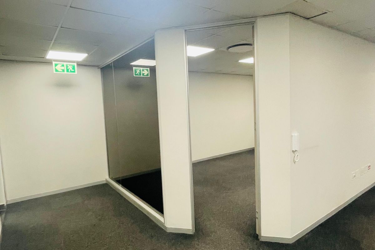 An empty office space featuring a suspended ceiling with recessed lighting, glass partitioning, and grey carpeting, suitable for a professional workspace.