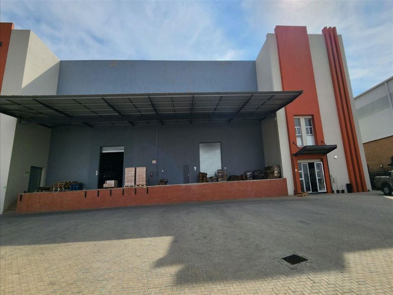 Industrial warehouse exterior featuring a raised loading dock, metal canopy, roller shutter access, and paved yard area.