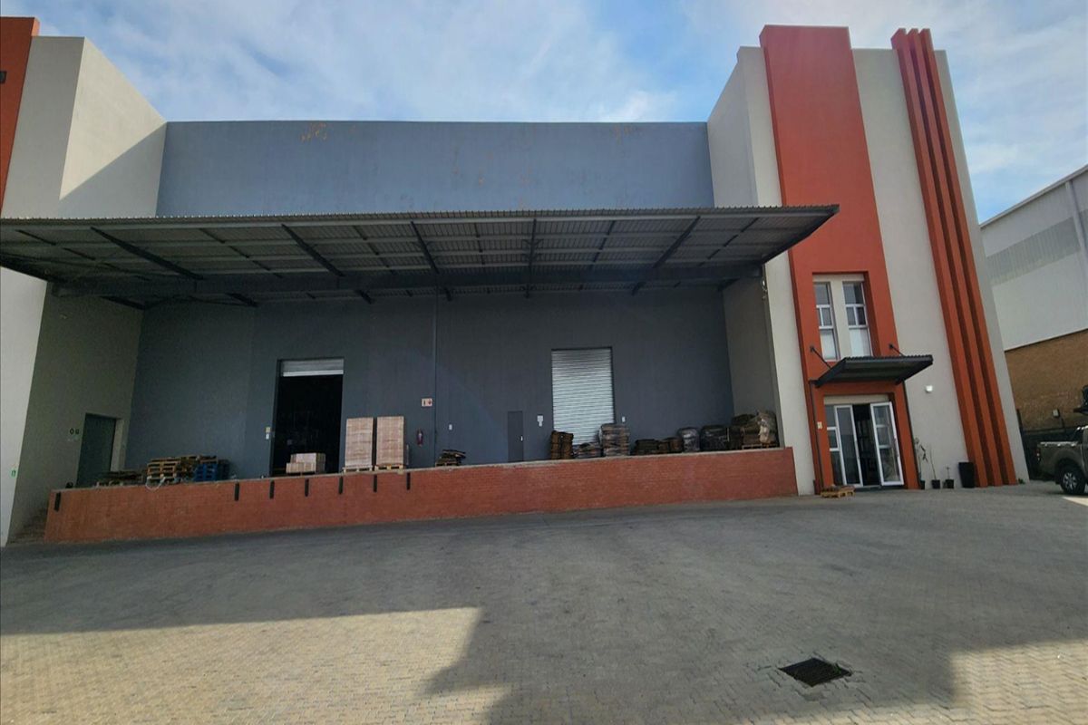 Industrial warehouse exterior featuring a raised loading dock, metal canopy, roller shutter access, and paved yard area.
