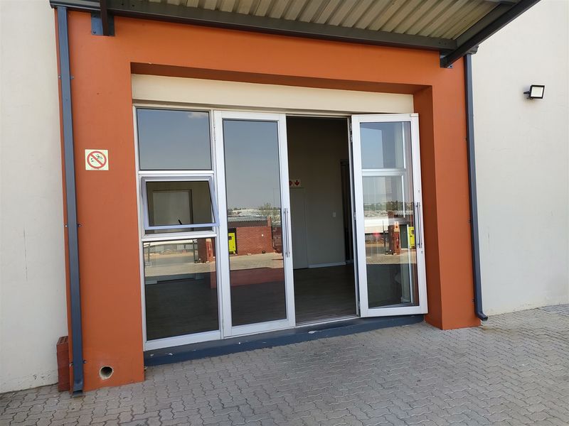 Industrial property entrance featuring modern aluminium-framed glass doors, a protective awning, and paved exterior access.
