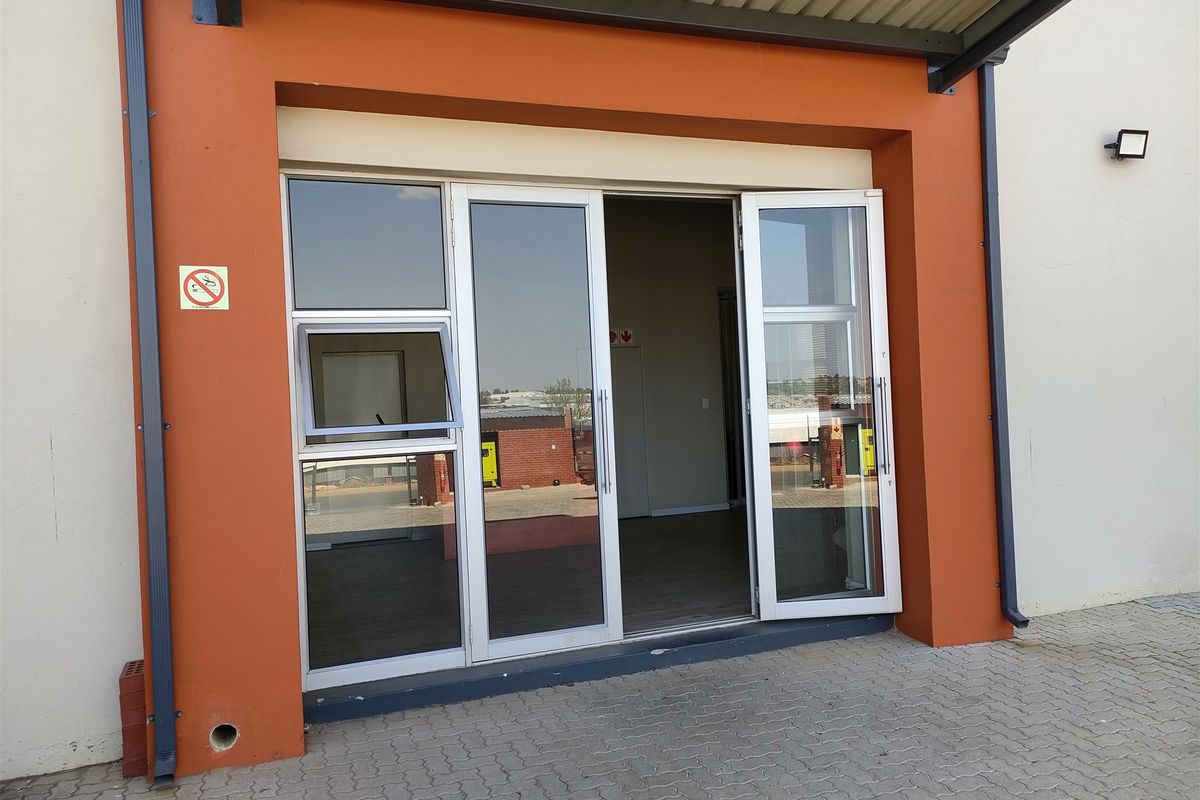 Industrial property entrance featuring modern aluminium-framed glass doors, a protective awning, and paved exterior access.