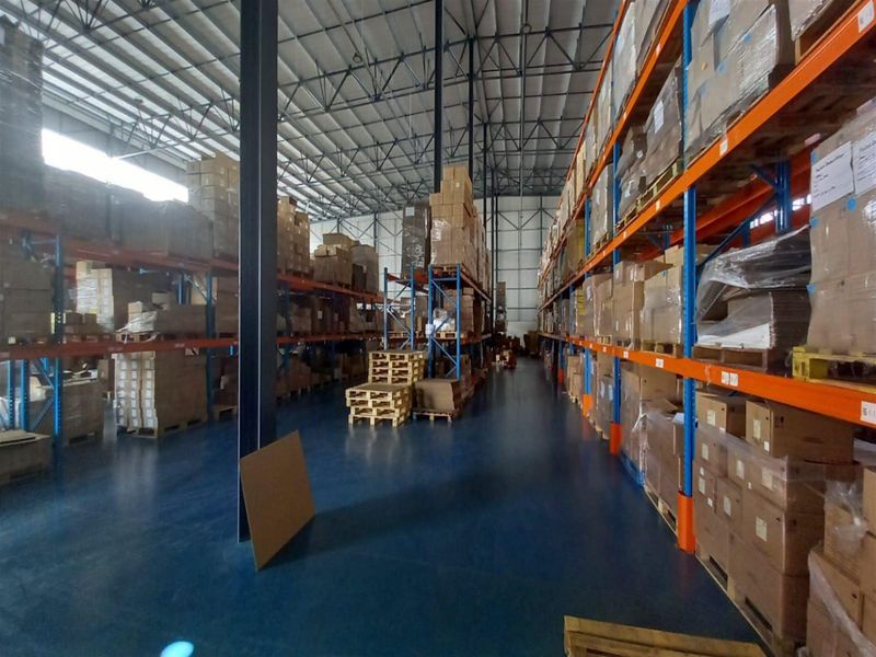 Spacious industrial warehouse featuring high ceilings with exposed steel trusses, durable epoxy-coated flooring, and extensive heavy-duty steel racking systems for storage.