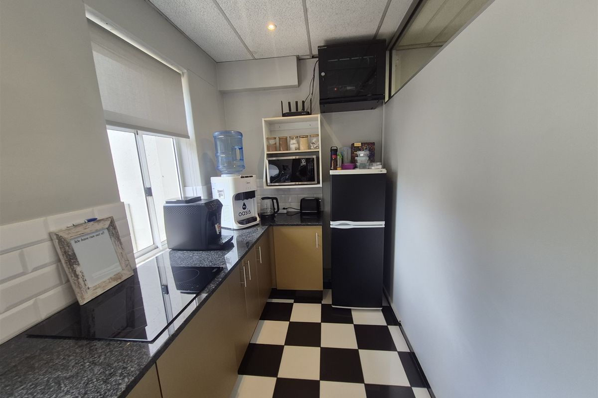 A compact office kitchenette featuring granite countertops, built-in cabinetry, a tiled backsplash, and a checkerboard vinyl floor.