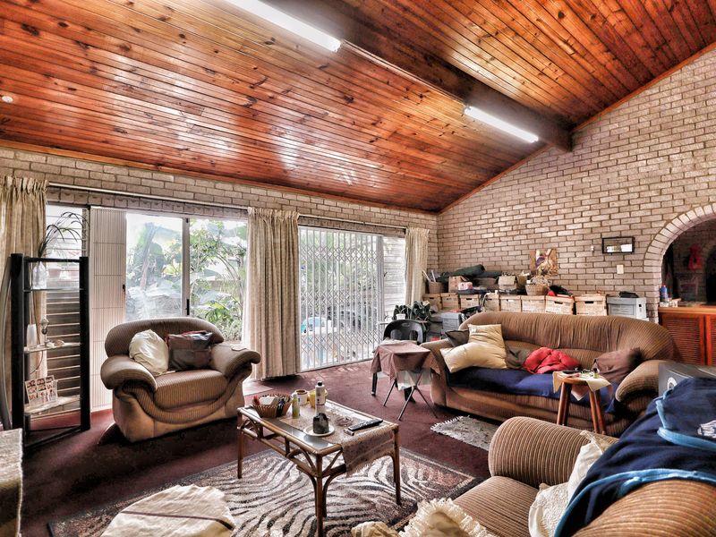 Spacious living area featuring a high raked timber ceiling, exposed brick walls, and large sliding glass doors providing access to the exterior.