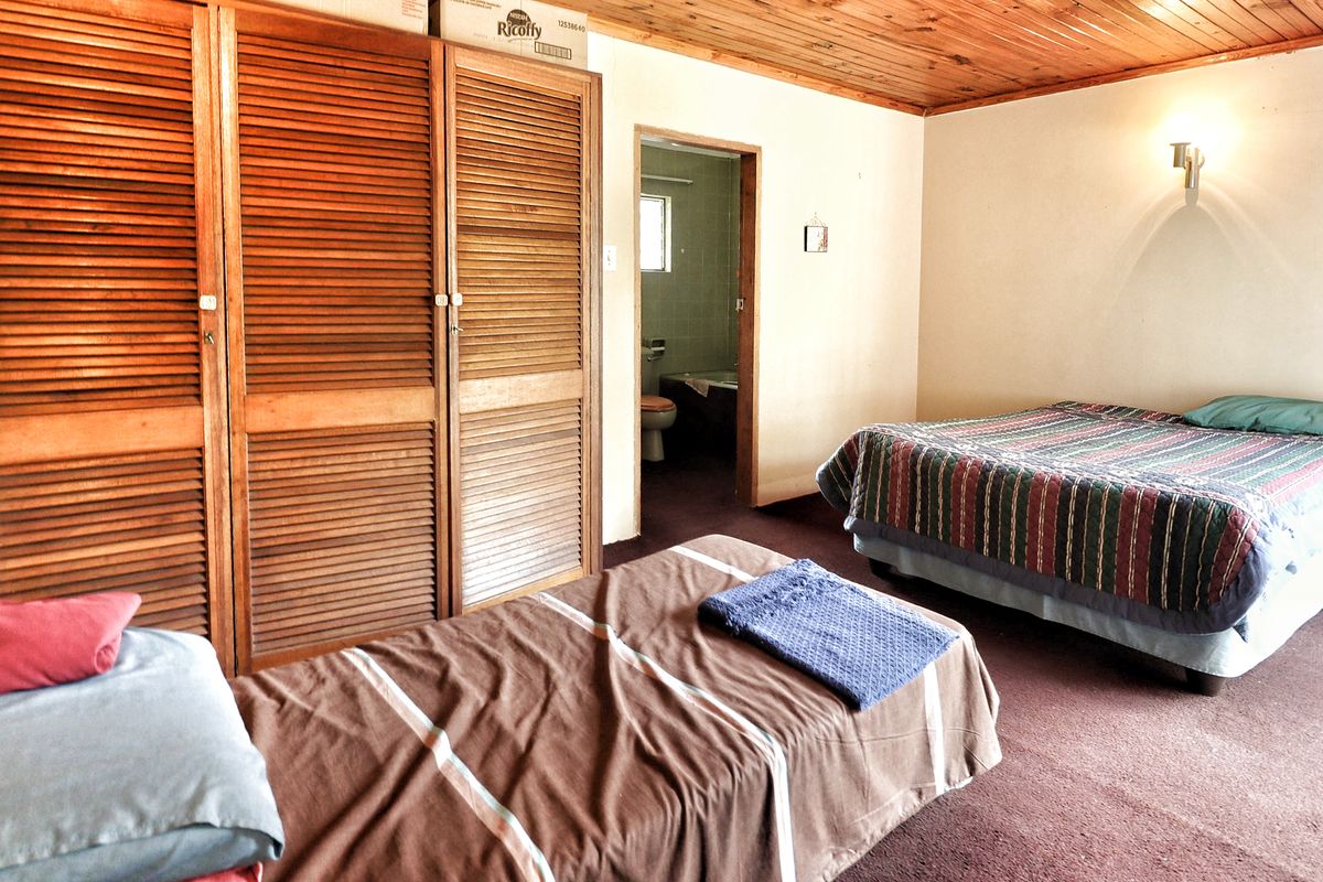 A bedroom featuring built-in wooden louvered cupboards, a timber plank ceiling, and an en-suite bathroom access.