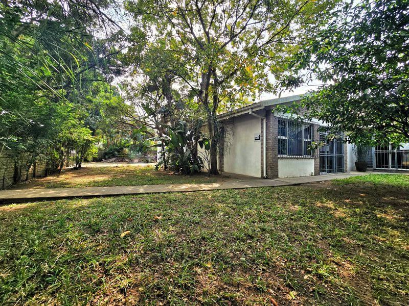 Rear view of the office building featuring a concrete walkway, established trees, and security bars on the windows.