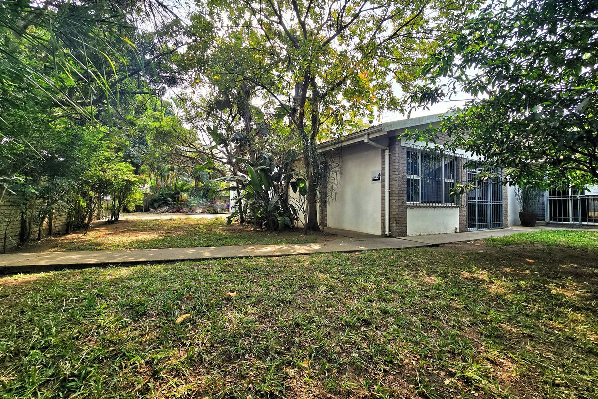 Rear view of the office building featuring a concrete walkway, established trees, and security bars on the windows.