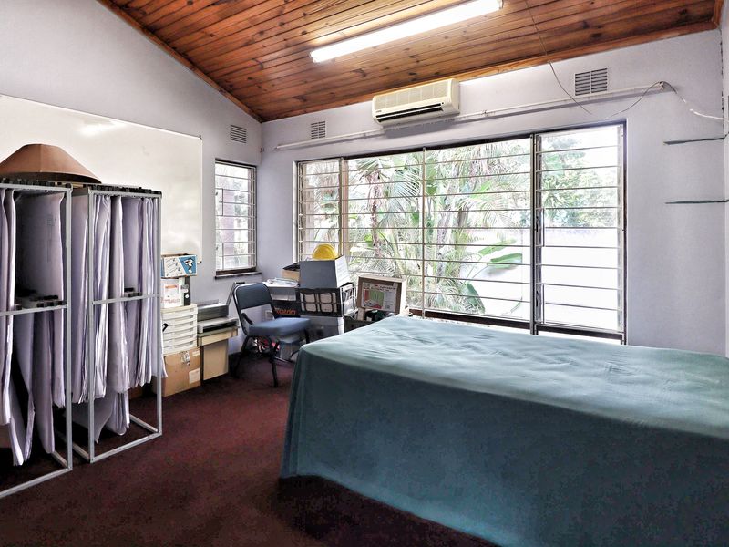 Office space featuring a timber-clad vaulted ceiling, large windows with security bars, and a wall-mounted air conditioning unit.