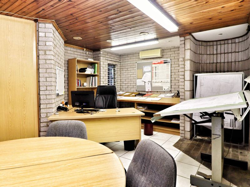 A functional office space featuring exposed brick walls, timber ceiling paneling, and tiled flooring, equipped with built-in storage and air conditioning.