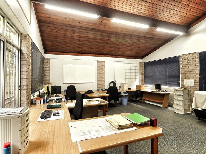 Spacious office area featuring exposed timber vaulted ceilings, brick wall accents, large windows with security bars, and integrated whiteboard installations.