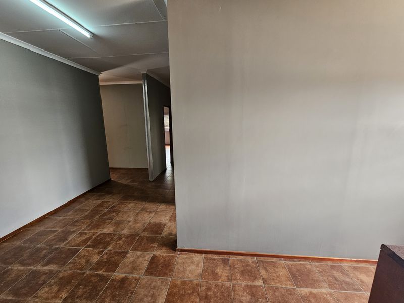 An empty office space featuring ceramic floor tiles, neutral painted walls, and overhead fluorescent lighting, providing a functional layout for professional use.