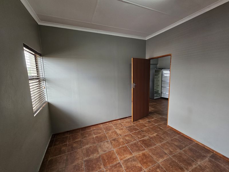 A vacant office space featuring neutral grey walls, tiled flooring, and venetian blinds, offering a clean and functional environment for professional use.