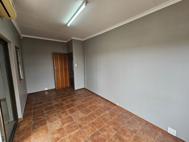 A vacant office space featuring tiled flooring, grey walls, a ceiling-mounted light fixture, and an integrated air conditioning unit.