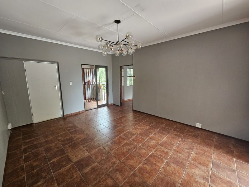 An empty office space featuring tiled flooring, a modern chandelier, and access to an outdoor area through a sliding door with a security gate.