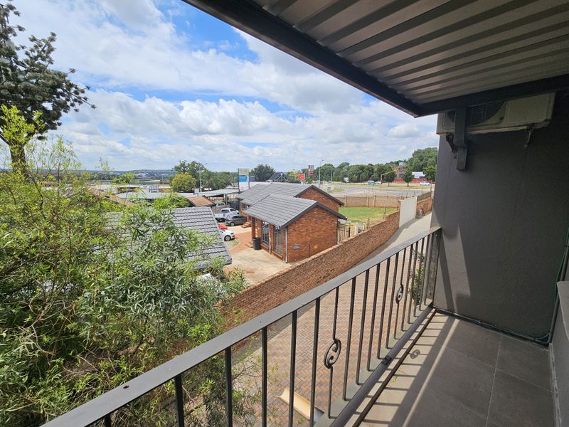 A covered balcony with metal railings and tiled flooring, offering an elevated view of the surrounding office park and neighborhood.