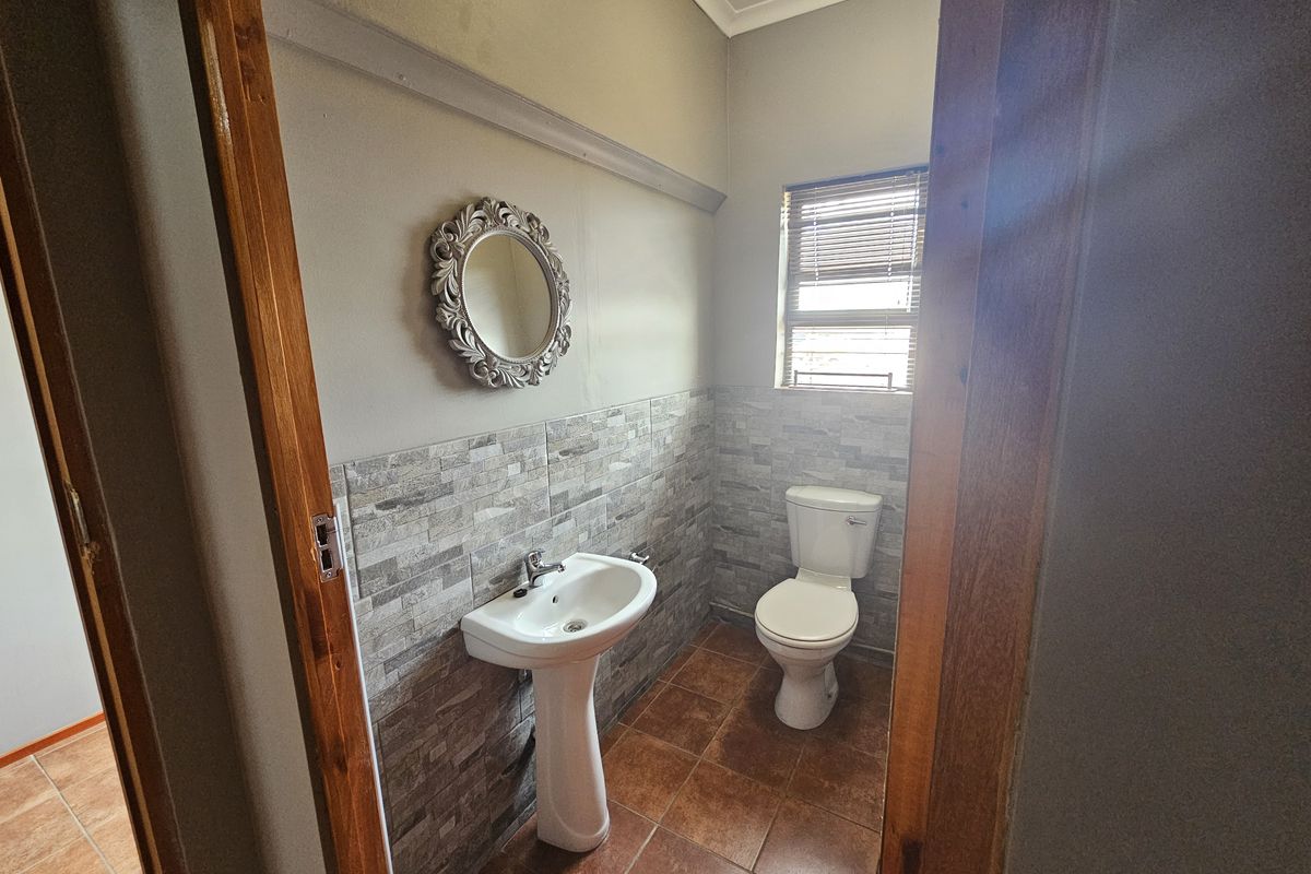 A functional office bathroom featuring a pedestal basin, toilet, tiled splashback, and tiled flooring with natural light from a window.
