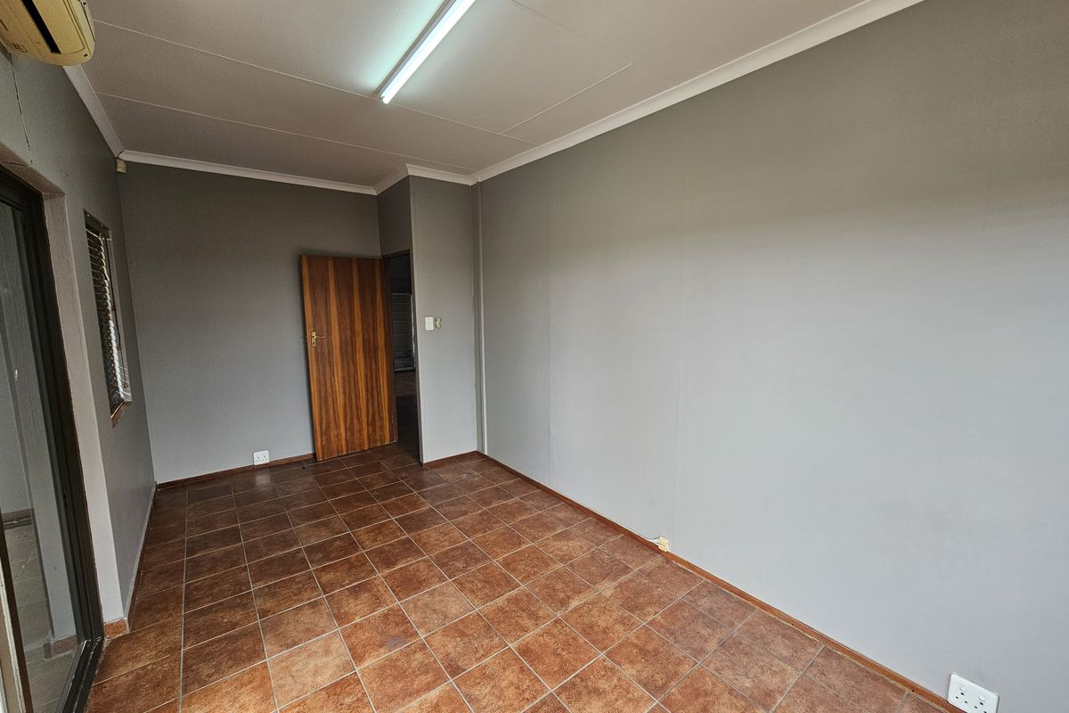 A vacant office space featuring tiled flooring, grey walls, a ceiling-mounted light fixture, and an integrated air conditioning unit.