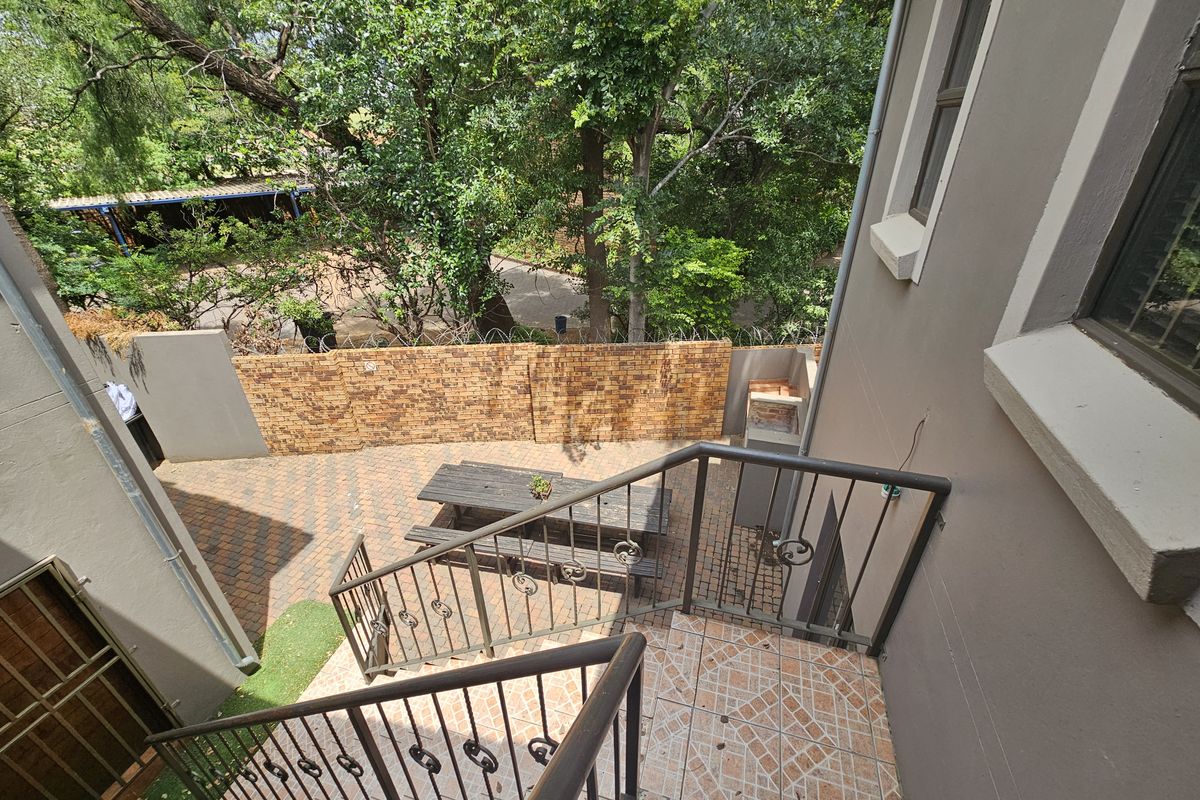 An elevated view of a rear courtyard featuring a paved patio area, built-in braai, and a metal staircase leading down from the building.