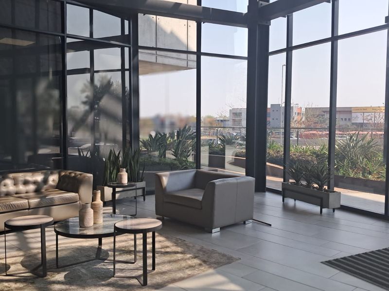 Modern office lounge area featuring expansive floor-to-ceiling windows, sleek black metal framing, and high-quality large format floor tiles with abundant natural light.