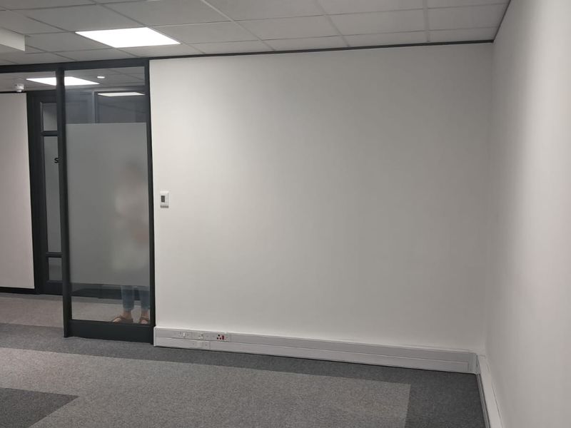 A clean, modern office space featuring neutral carpet tiles, a suspended ceiling with recessed lighting, and a glass partition wall.