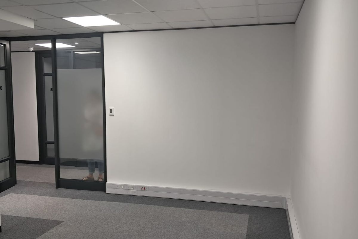 A clean, modern office space featuring neutral carpet tiles, a suspended ceiling with recessed lighting, and a glass partition wall.