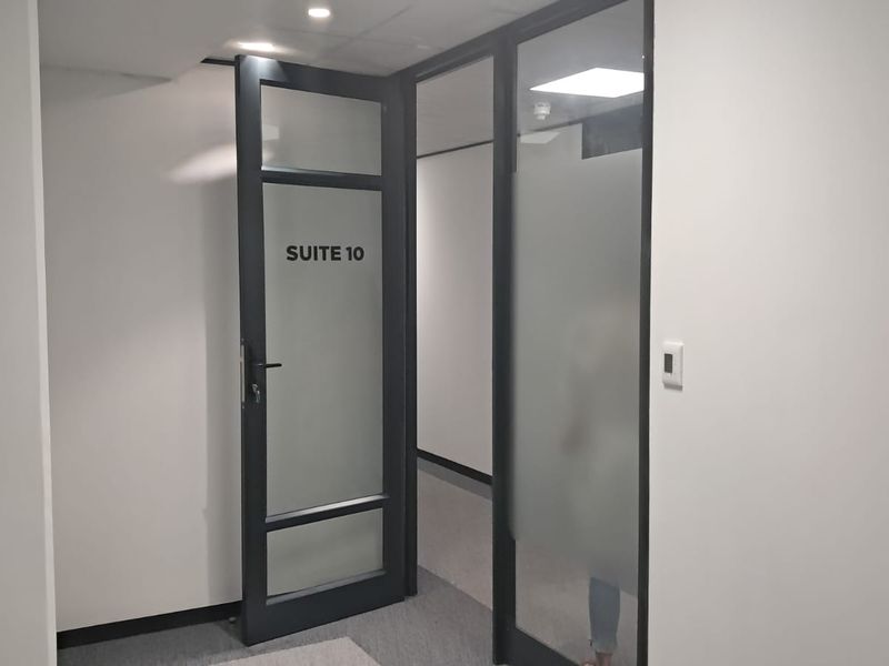 A clean, modern office hallway featuring frosted glass suite doors with black frames and recessed ceiling lighting.