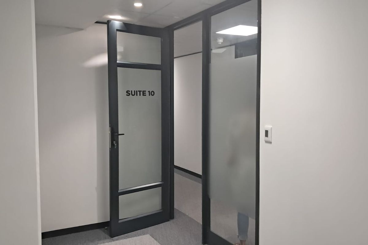 A clean, modern office hallway featuring frosted glass suite doors with black frames and recessed ceiling lighting.