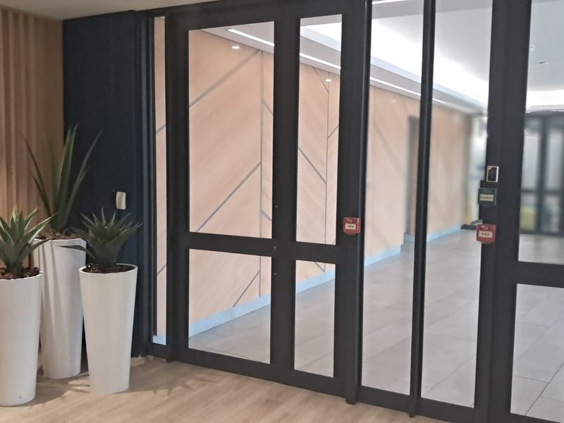 Modern office entrance featuring sleek glass partition doors, timber slat wall detailing, and professional access control systems.