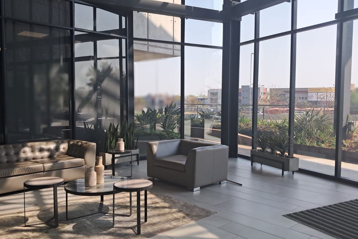 Modern office lounge area featuring expansive floor-to-ceiling windows, sleek black metal framing, and high-quality large format floor tiles with abundant natural light.