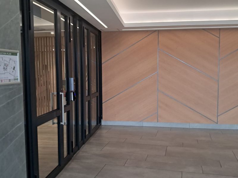 Modern office entrance lobby featuring high-quality timber veneer wall paneling, large glass doors, and sleek tiled flooring with recessed ceiling lighting.