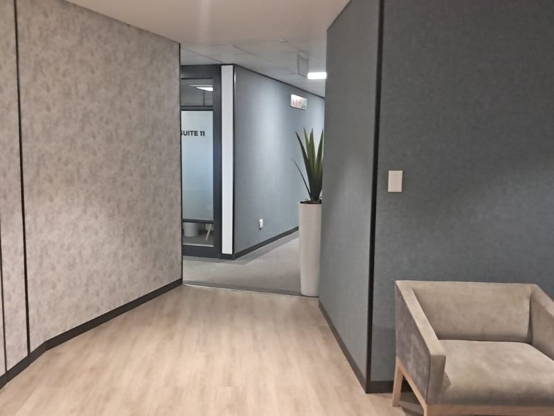 A modern office hallway featuring laminate flooring, textured wall finishes, and a glass-partitioned entrance to Suite 11.