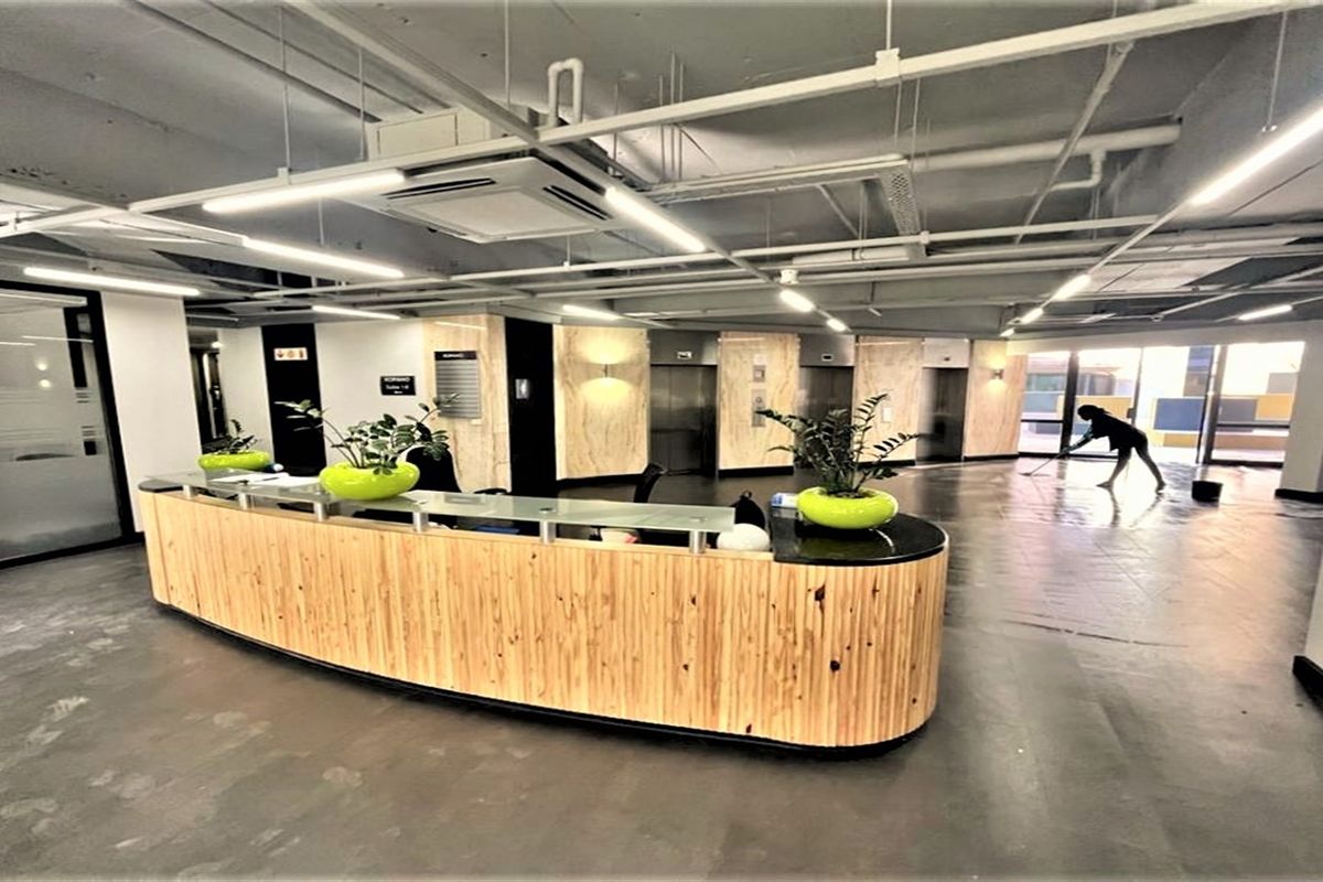 Modern office reception area featuring a curved wooden desk, exposed industrial-style ceiling, and integrated elevator access.