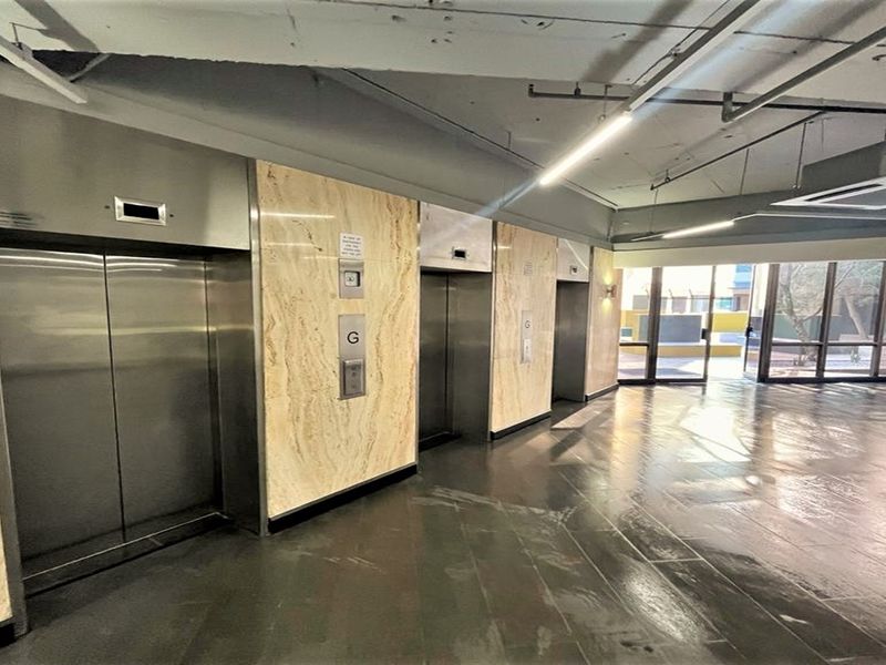 Modern office building lobby featuring marble-clad elevator banks, polished tile flooring, and an industrial-style exposed ceiling with integrated lighting.