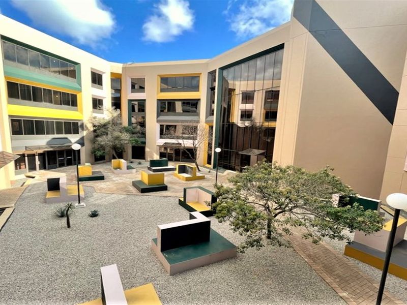 A modern multi-story office building featuring a central courtyard with paved areas, built-in concrete seating, and large glass facade elements.