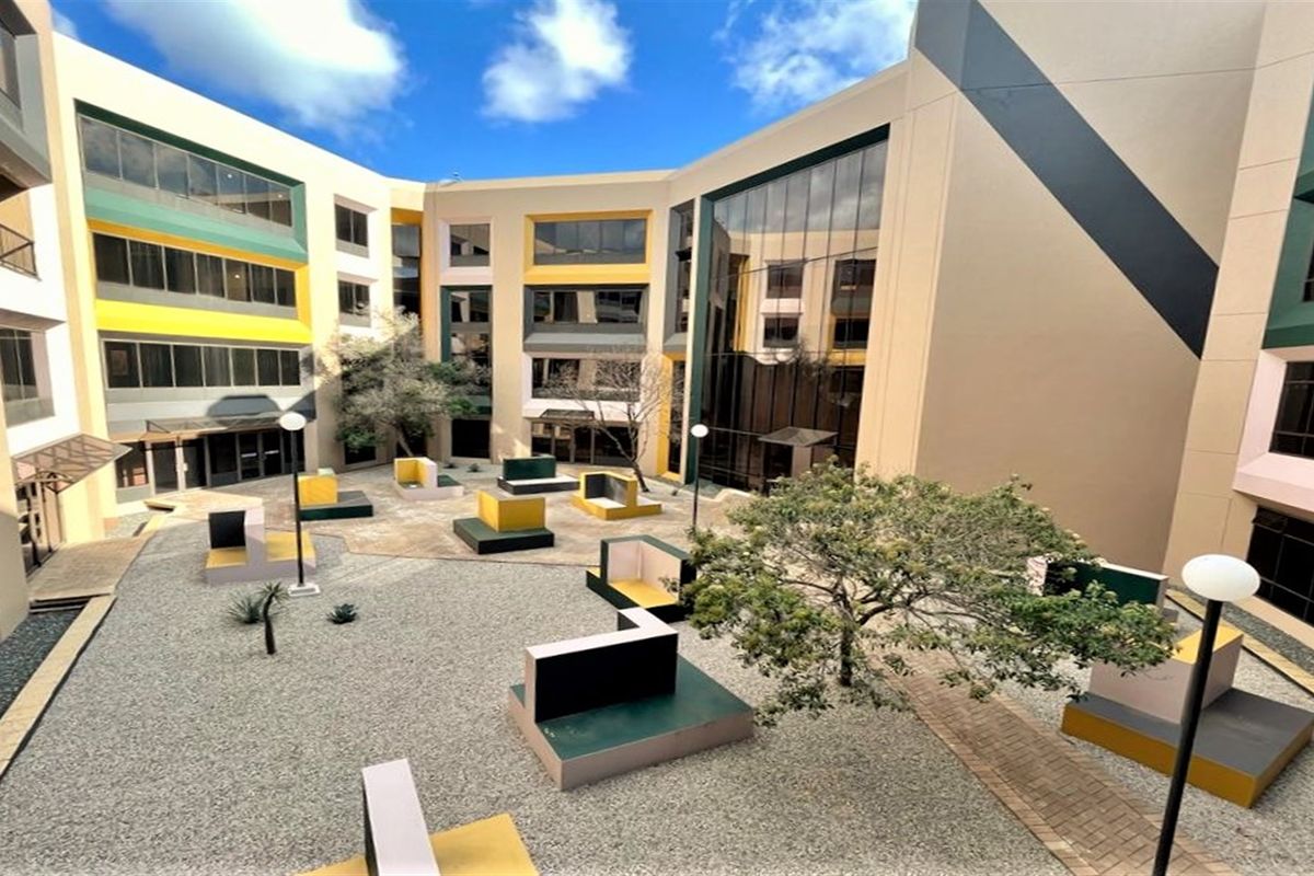 A modern multi-story office building featuring a central courtyard with paved areas, built-in concrete seating, and large glass facade elements.
