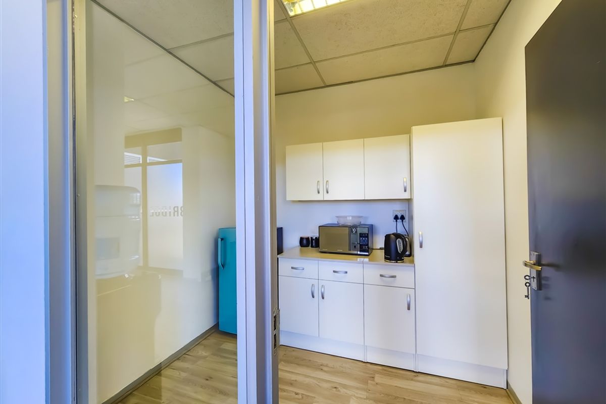 A compact office kitchenette featuring white cabinetry, laminate flooring, and a drop ceiling with integrated lighting.