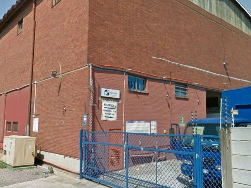 Exterior view of an industrial warehouse building featuring brick construction, secure gated access, and perimeter security fencing.