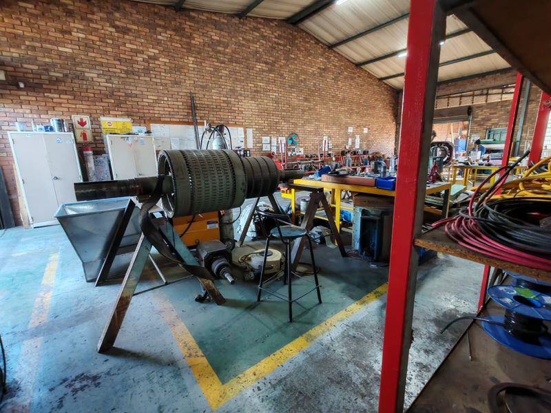 Industrial workshop space featuring exposed brick walls, high ceilings with steel trusses, and durable painted concrete flooring, suitable for manufacturing or repair operations.