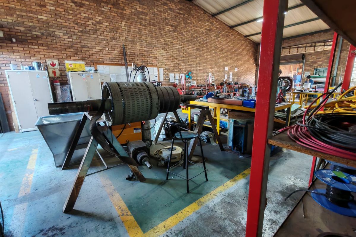 Industrial workshop space featuring exposed brick walls, high ceilings with steel trusses, and durable painted concrete flooring, suitable for manufacturing or repair operations.