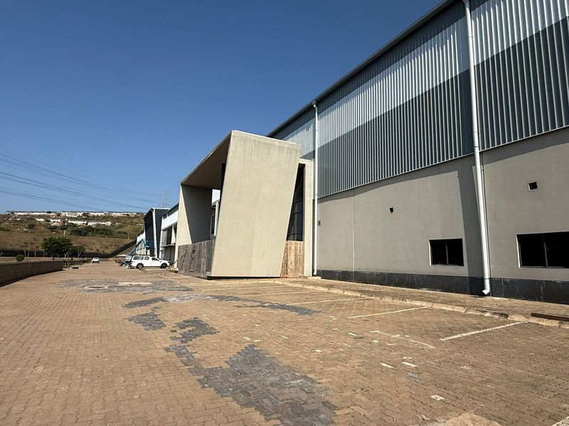 Exterior view of an industrial warehouse facility featuring a concrete entrance facade, corrugated metal cladding, and a paved parking area.