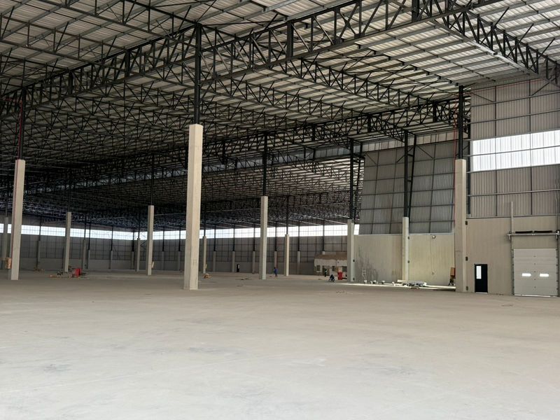 A large, open-plan industrial warehouse space featuring high ceilings with exposed steel trusses, polished concrete flooring, and a large roller shutter door.