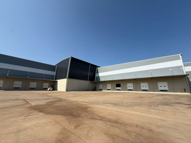 Large industrial warehouse exterior featuring multiple loading docks with roller shutter doors and a spacious concrete yard area.