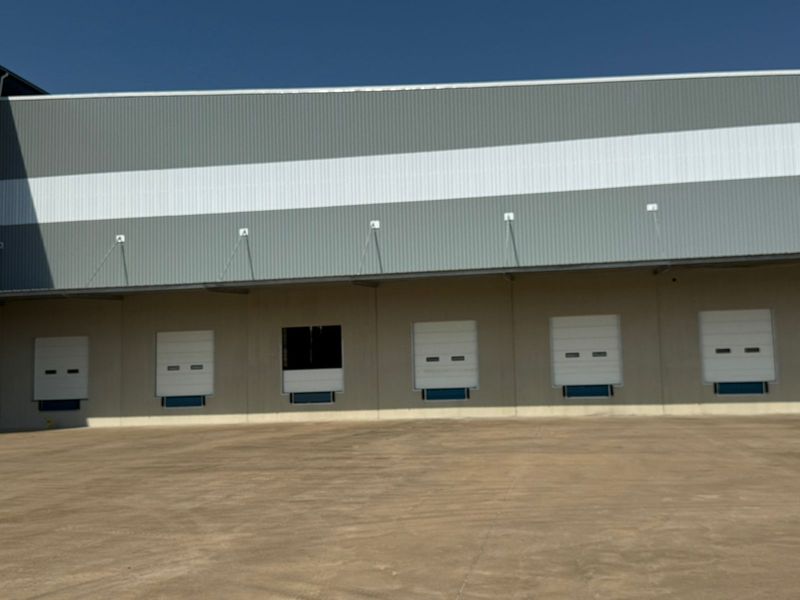 Industrial warehouse exterior featuring multiple loading dock doors and a large concrete yard area.