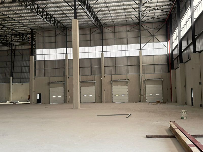 Spacious industrial warehouse interior featuring high ceilings, concrete flooring, and multiple roller shutter loading doors, suitable for logistics or manufacturing operations.
