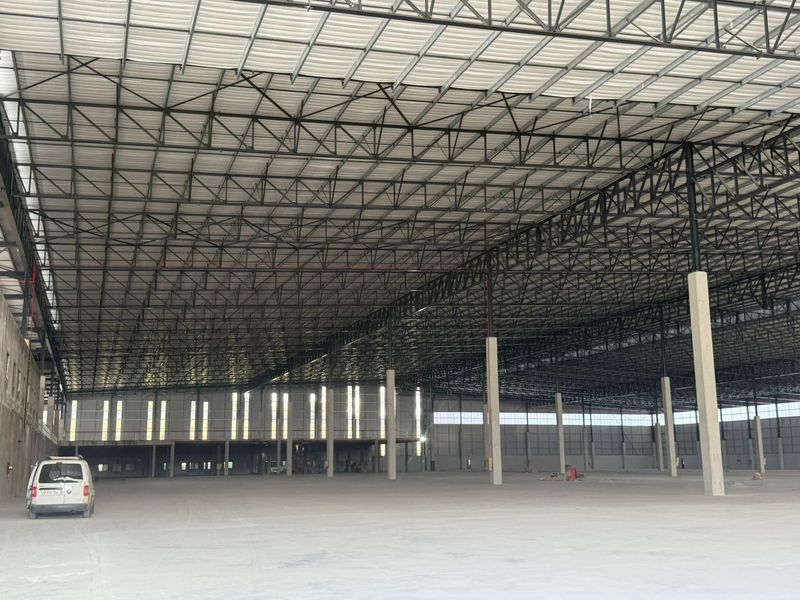Expansive industrial warehouse space featuring high-clearance steel truss roofing, concrete flooring, and structural support columns, suitable for large-scale storage or manufacturing operations.