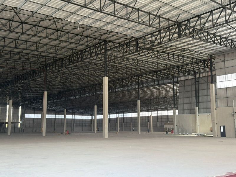 Expansive industrial warehouse space featuring high ceilings with exposed steel trusses, concrete flooring, and ample natural light through high-level windows.
