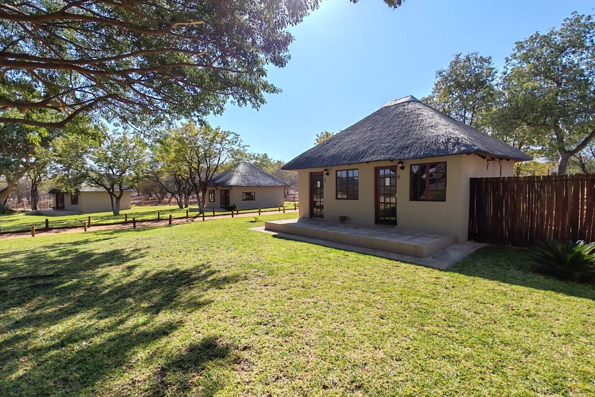 A view of well-maintained farm chalets featuring traditional thatch roofs, tiled patios, and expansive lawn areas surrounded by mature trees.