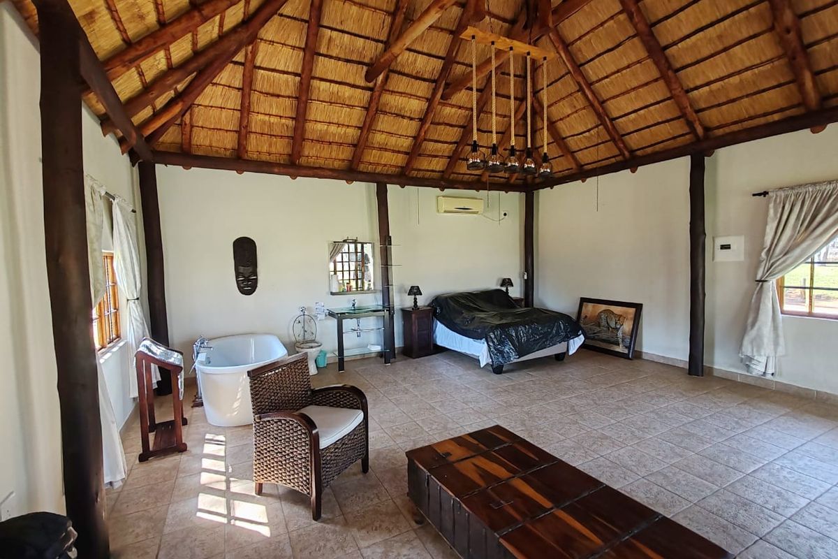 Spacious bedroom featuring a high thatched roof with exposed timber beams, tiled flooring, a freestanding bathtub, and an integrated air conditioning unit.